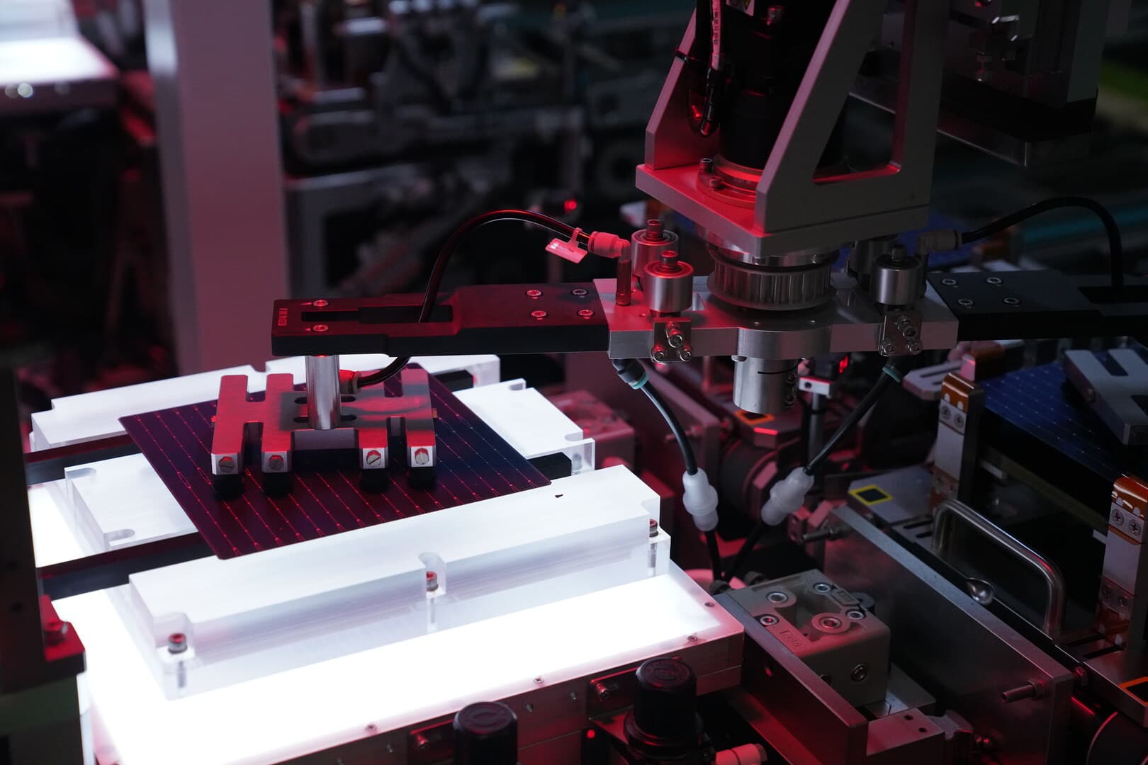 Robotic gripper lifting a TOPCon cell from a backlit alignment table